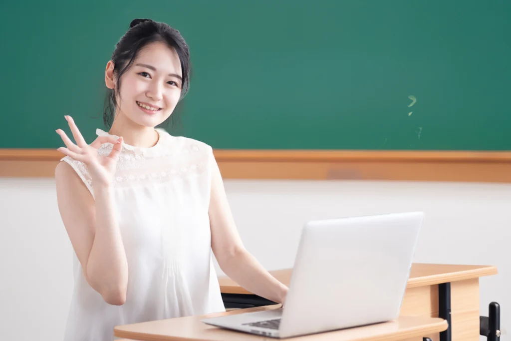 女性教師がパソコンを操作しながらOKポーズをしている